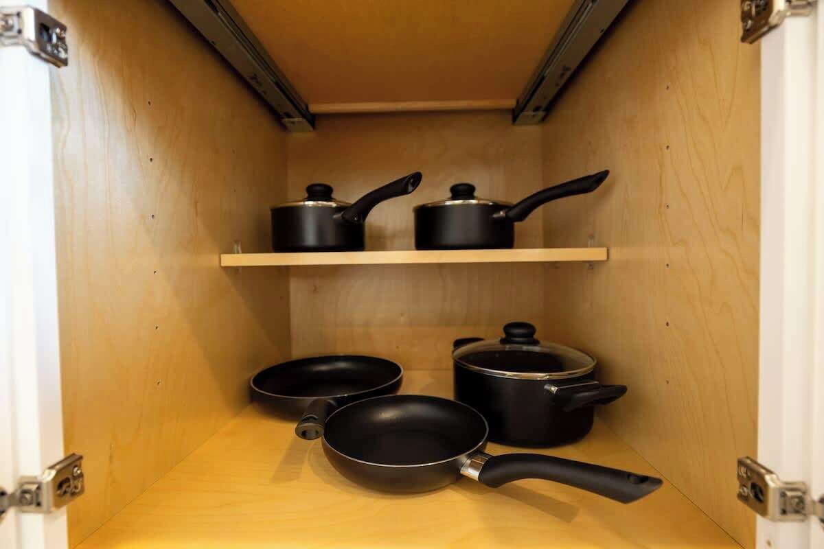 Un meuble en bois contenant des ustensiles de cuisine noirs, notamment une poêle, deux casseroles et une autre poêle sur l’étagère inférieure.