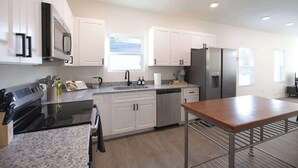 A modern kitchen with white cabinets, stainless steel appliances, and a wooden table. - 5 Min to Elon | 7 Min to Downtown | Washer + Dryer (Burlington)