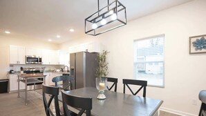 A modern kitchen with white cabinets, stainless steel appliances, and a dining area with a dark wooden table and chairs. - 5 Min to Elon | 7 Min to Downtown | Washer + Dryer (Burlington)
