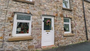 Une maison en pierre avec une porte blanche, une fen être ornée d’une guirlande et une petite fenêtre au-dessus de la porte.