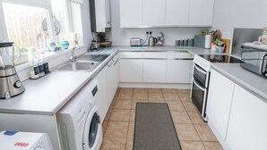 Une cuisine compacte équipée d’un lave-linge, d’un évier, d’une cuisinière et d’une fenêtre agrémentée d’un rideau à motifs.