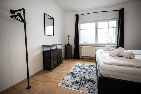 A bedroom with a bed, a dresser, a mirror, a window with curtains, and a floor lamp. - Mountaineer sleeping places | Parking & Wifi (Kempten (Allgäu))