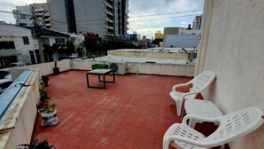 Una terrazza sul tetto con pavimento rosso, sedie di plastica bianca, un tavolino e piante in vaso.
