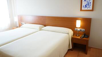 A hotel room with two beds, a nightstand with a lamp, a phone, and a framed picture on the wall.