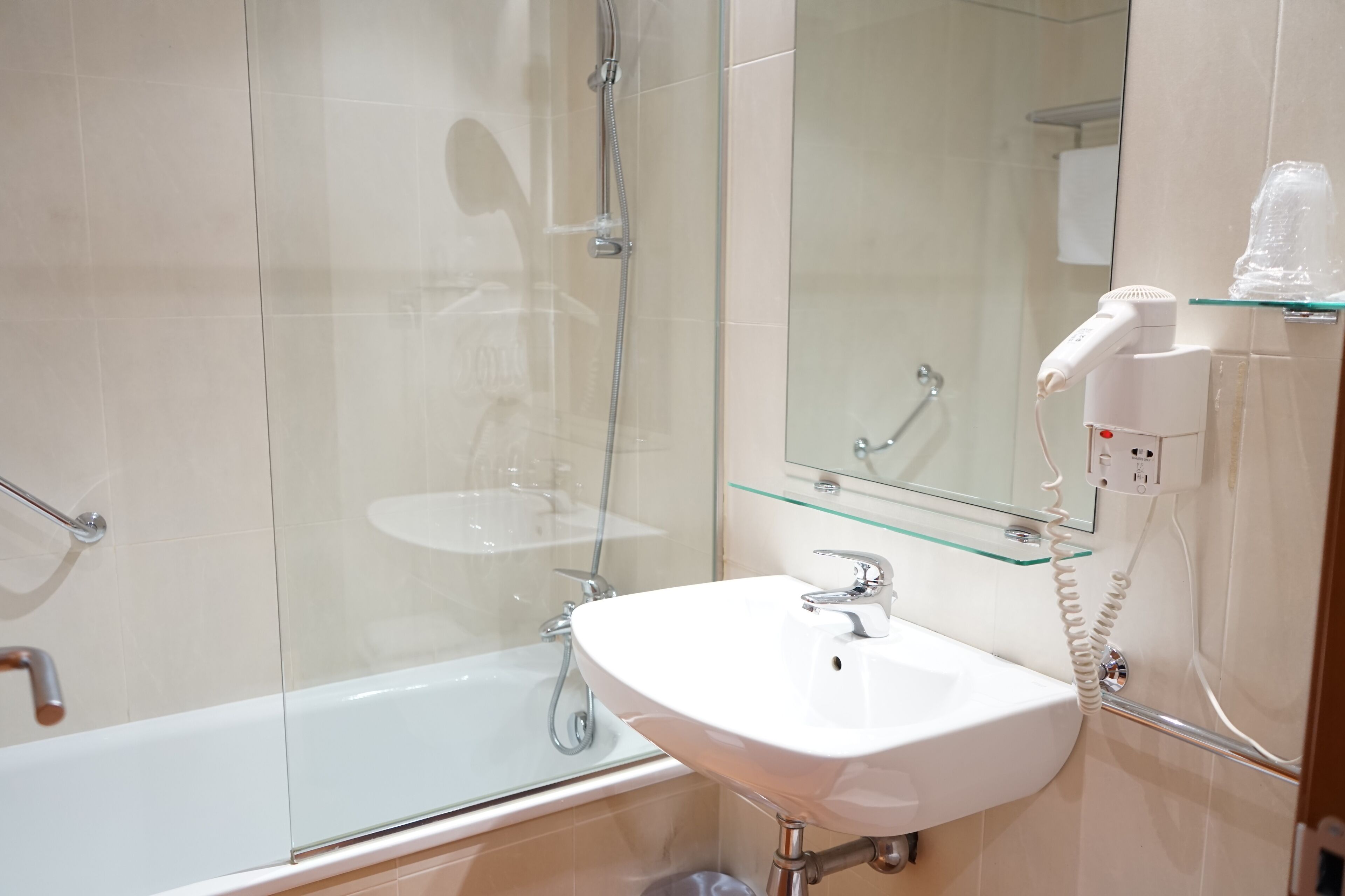 A modern bathroom with a glass shower enclosure, a white sink, and a hairdryer on a glass shelf.