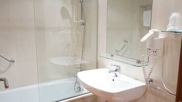 A modern bathroom with a glass shower enclosure, a white sink, and a hairdryer on a glass shelf.