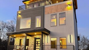 A modern two-story house with a stone facade, large windows, and a covered porch. - Luxe Pigeon Forge Cabin | Golf Sim + Hot Tub (Pigeon Forge)