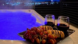 A hot tub with a city view at night, a tray of grapes, and two glasses of red wine. - Luxe Pigeon Forge Cabin | Golf Sim + Hot Tub (Pigeon Forge)