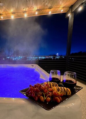Ein Whirlpool mit Stadtblick bei Nacht, eine Schale Trauben und zwei Gläser Rotwein.