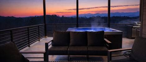 Ein Balkon mit Whirlpool, einer Couch und Stühlen, mit Blick auf eine Berglandschaft bei Sonnenuntergang.