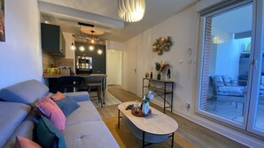 A modern living room with a grey sofa, a coffee table, and a dining area with a kitchen in the background. - Le Jungle - 2p - Blagnac (Blagnac)