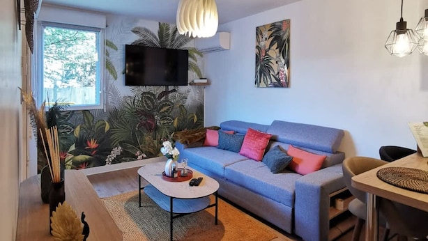 A modern living room with a blue sofa, a coffee table, and a TV mounted on the wall. - Le Jungle - 2p - Blagnac (Blagnac)