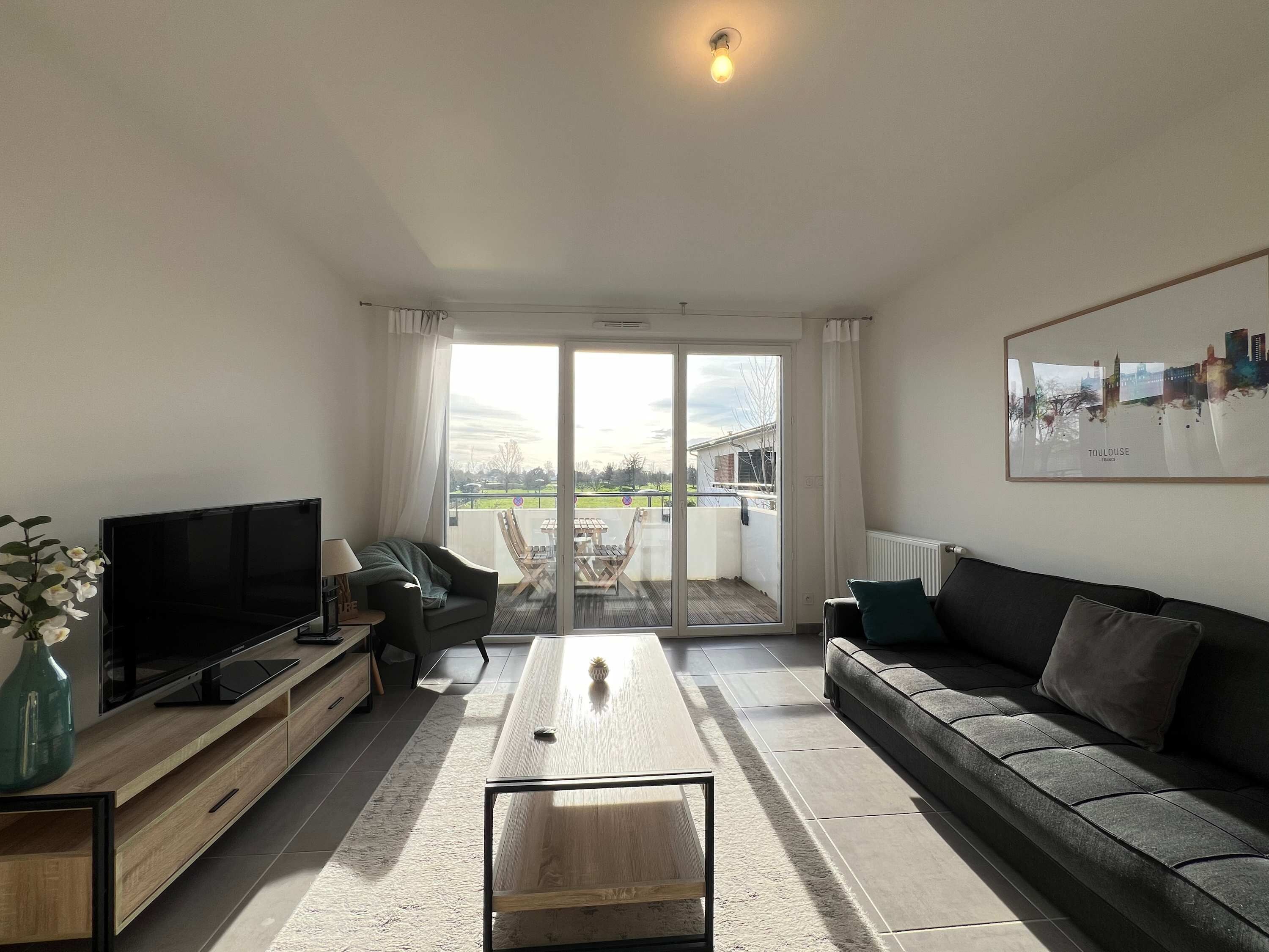Ein modernes Wohnzimmer mit Flachbildfernseher, einer Couch, einem Couchtisch und einer Glasschiebetür, die zu einer Außenpatio führt.
