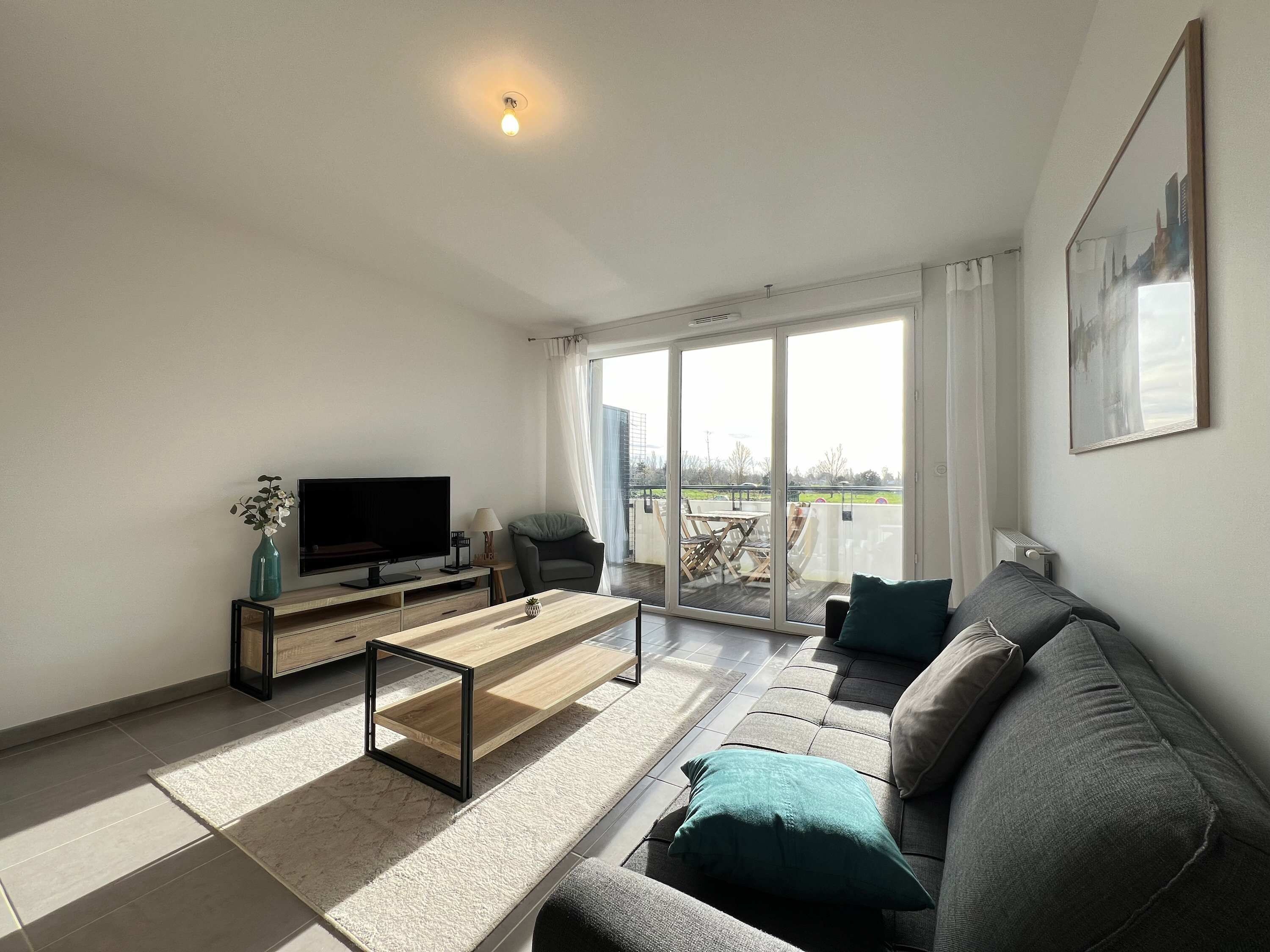 A modern living room with a flat-screen TV, a sofa, a coffee table, and a sliding glass door leading to an outdoor patio.