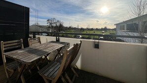 Un patio exterior con una mesa y sillas de madera, con vista a un campo verde y un edificio.