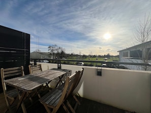 Un patio exterior con una mesa y sillas de madera, con vista a un campo verde y un edificio.