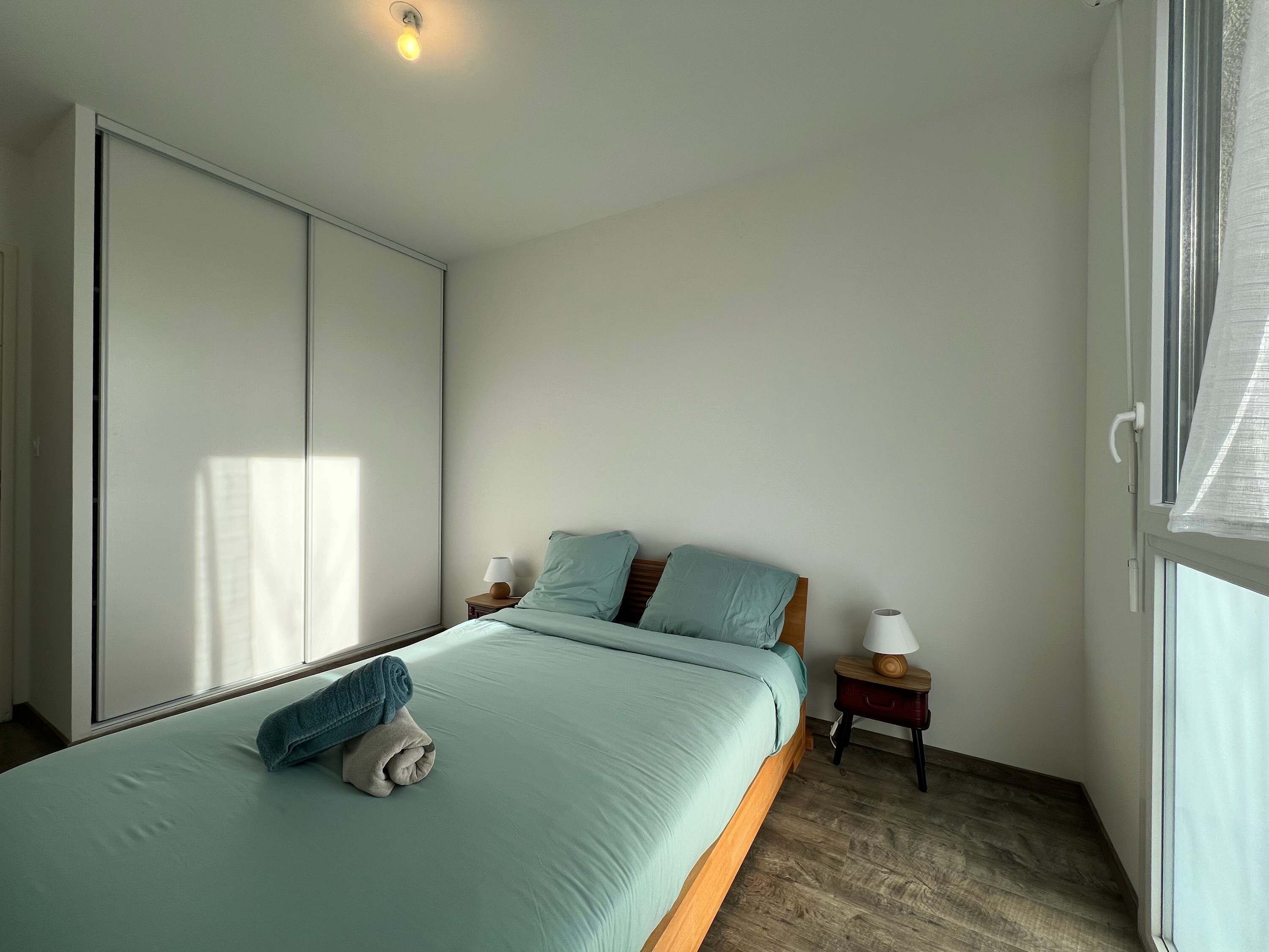 A bedroom with a bed, two bedside tables, a window, and a wardrobe.