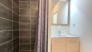 Un baño moderno con paredes de azulejos oscuros, cortina de ducha, lavamanos y espejo.