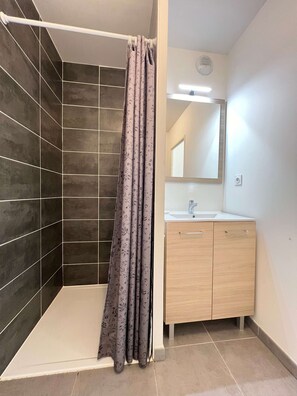 Un baño moderno con paredes de azulejos oscuros, cortina de ducha, lavamanos y espejo.