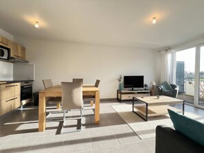 A modern living room with a dining area, a TV, and a balcony with a view. - Le Lamartine - 4p - Bords de Lac - Parking (Frouzins)