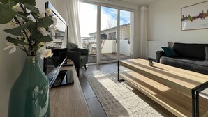 Una sala de estar moderna con un sofá, una mesa de centro y un televisor. Hay un ventanal con vistas al exterior.