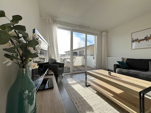 Una sala de estar moderna con un sofá, una mesa de centro y un televisor. Hay un ventanal con vistas al exterior.