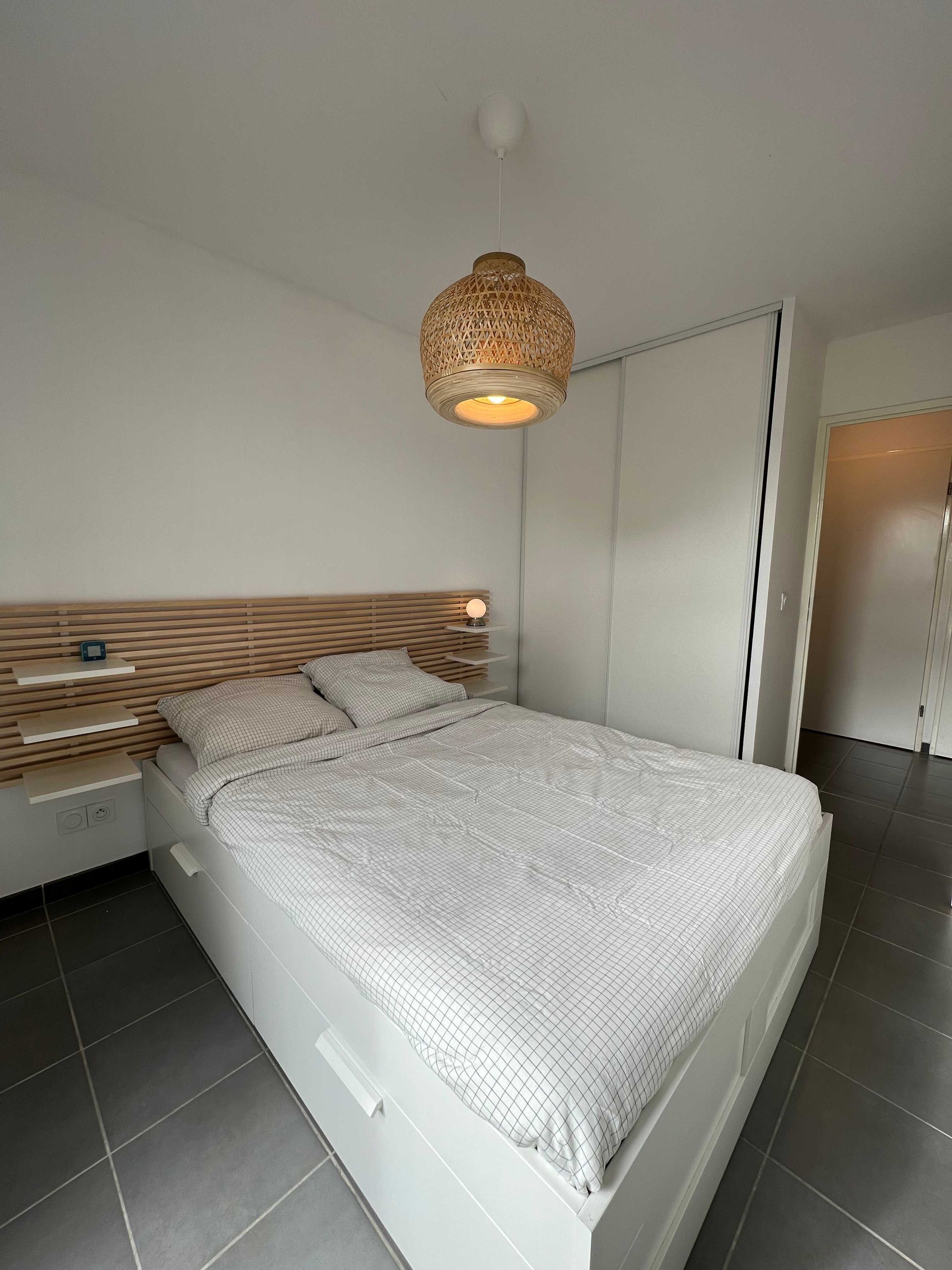 Een moderne slaapkamer met een groot bed, een houten hoofdbord, nachtkastjes en een hanglamp.