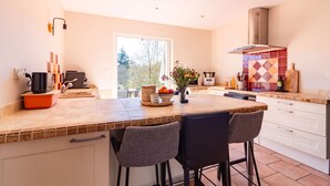 A modern kitchen with a large island, bar stools, a built-in oven, and a view of the outdoors. - La Tendresse - 10p - Piscine - Jardin (Mondonville)