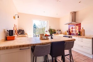 A modern kitchen with a large island, bar stools, a built-in oven, and a view of the outdoors.
