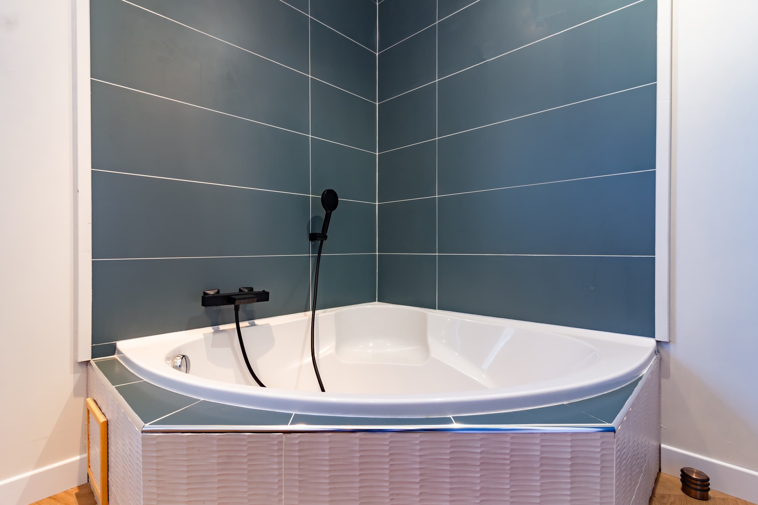 A modern bathroom with a freestanding bathtub, tiled walls, and a wooden floor.