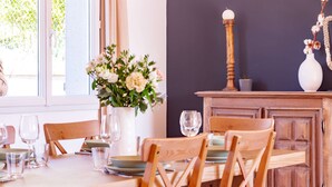 A dining area with a wooden table set for four, surrounded by wooden chairs. A vase with flowers is on the table, and a wooden cabinet is in the background. - La Tendresse - 10p - Piscine - Jardin (Mondonville)