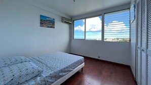 A bedroom with a bed, a window with a city view, and an air conditioning unit.