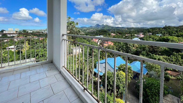 A balcony with a view of a mountainous landscape, a clear sky, and residential buildings in the distance.