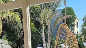 A wooden table with a bowl of fruit and a glass of juice, a hanging chair, and a pool in the background. - Complejo Pelicano Chapadmalal (Colonia Chapadmalal)