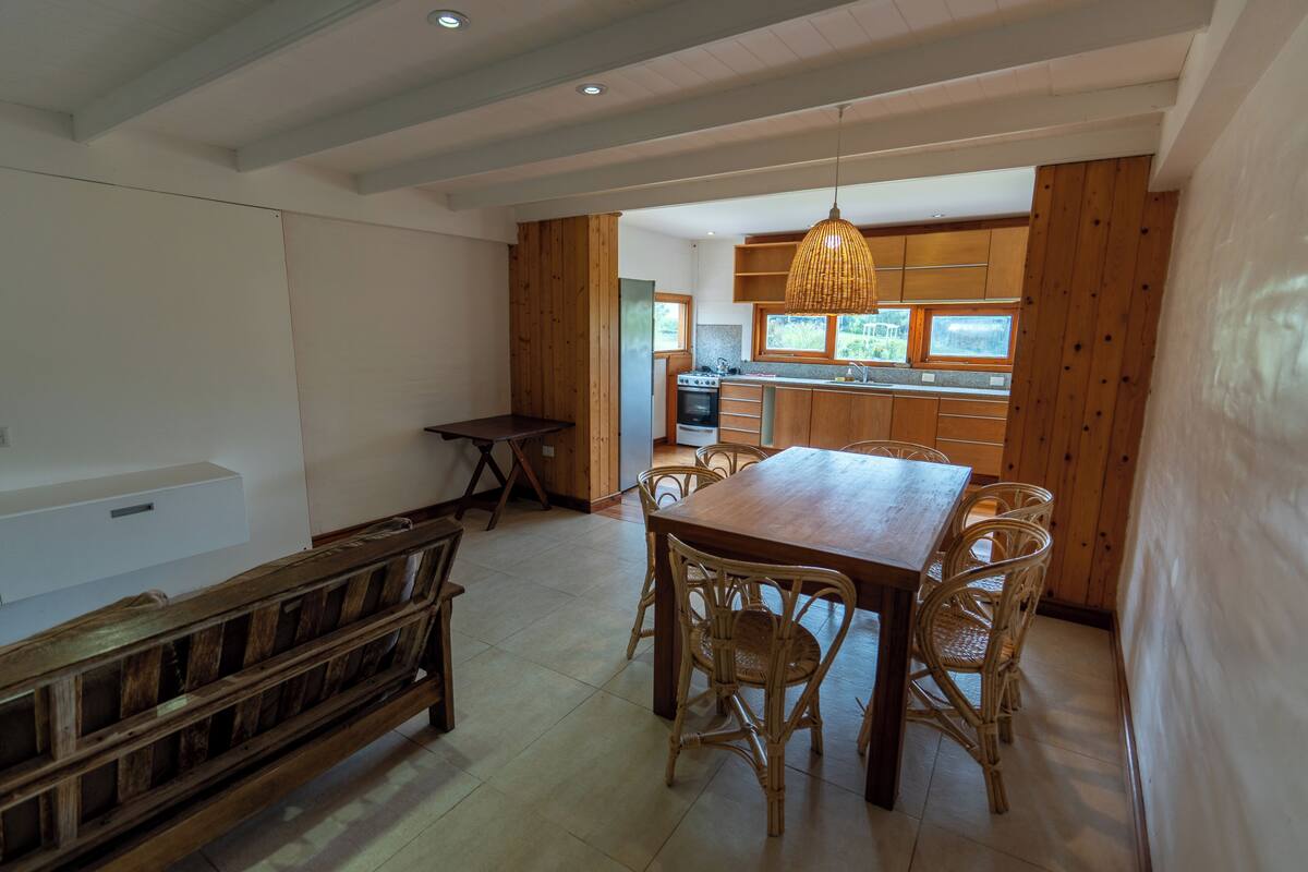 Un grand espace à manger avec une table et des chaises en bois, un banc et une cuisine en arrière-plan.