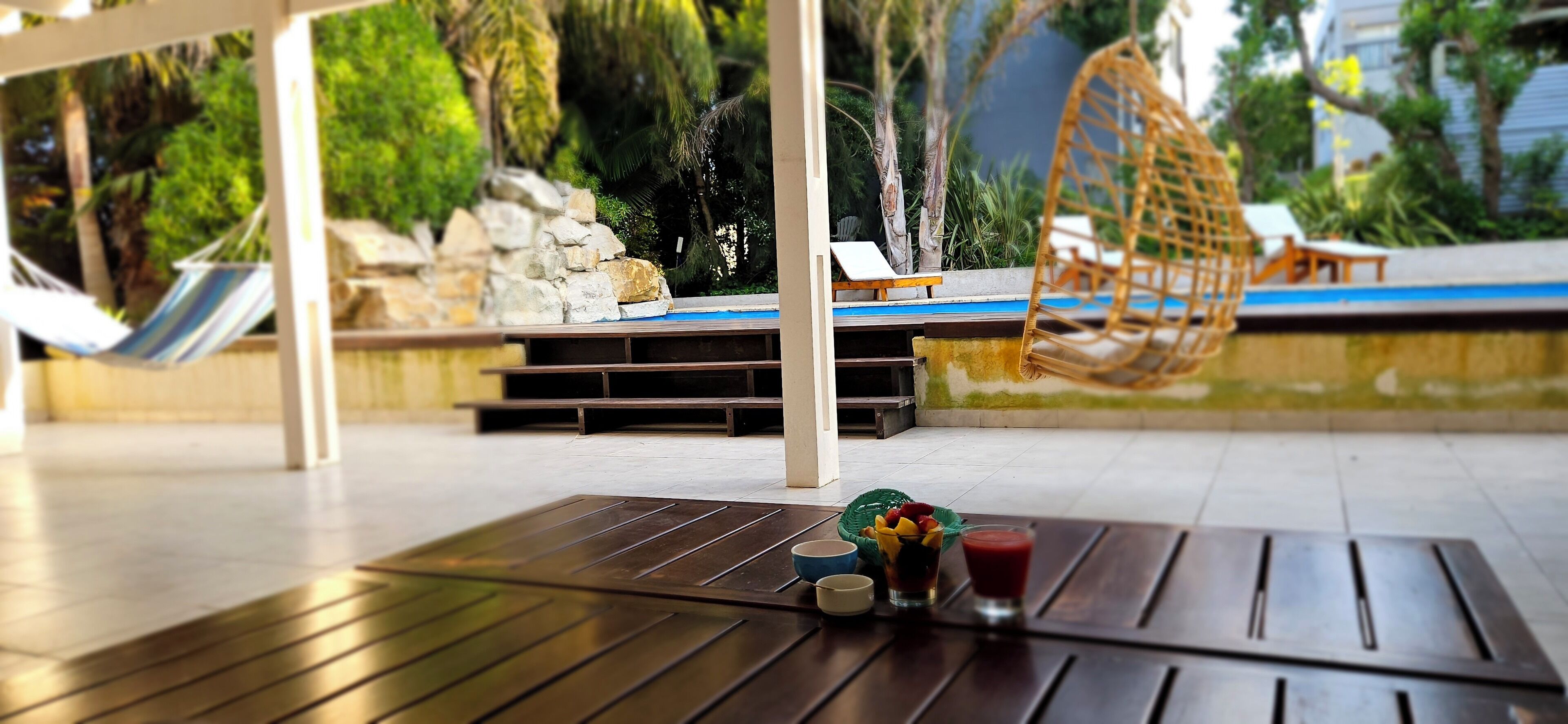 Una terraza de madera con una mesa, una hamaca y un área de piscina con sillones de descanso y un columpio.