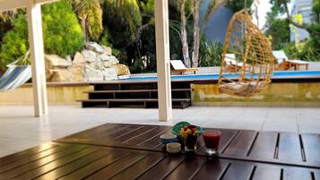 Una terraza de madera con una mesa, una hamaca y un área de piscina con sillones de descanso y un columpio.