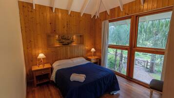 Een slaapkamer met houten lambrisering, een bed, nachtkastjes en een raam met uitzicht op groen.