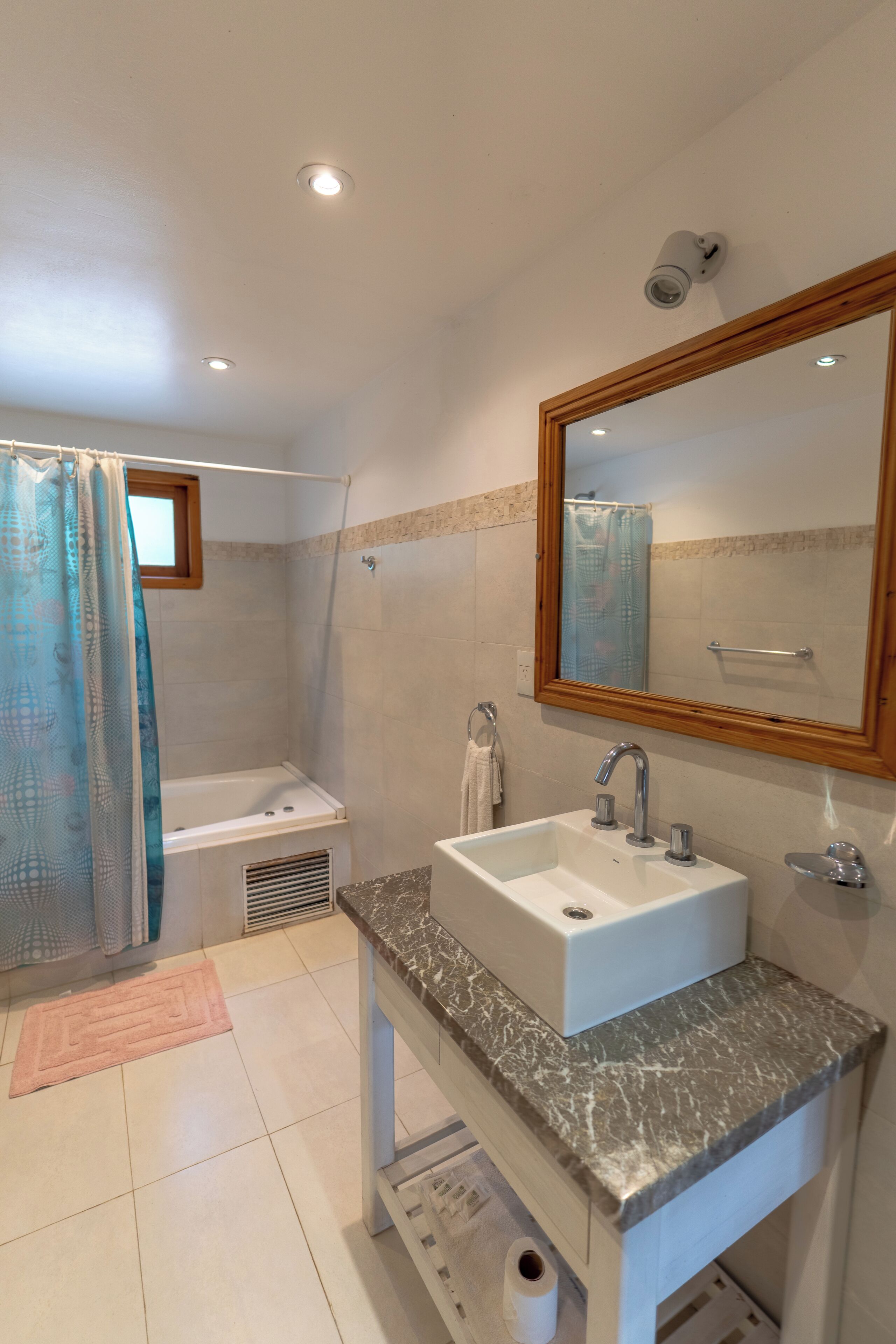 A bathroom with a bathtub, a sink with a marble countertop, a large mirror, and a shower curtain.