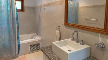 A bathroom with a bathtub, a sink with a marble countertop, a large mirror, and a shower curtain.
