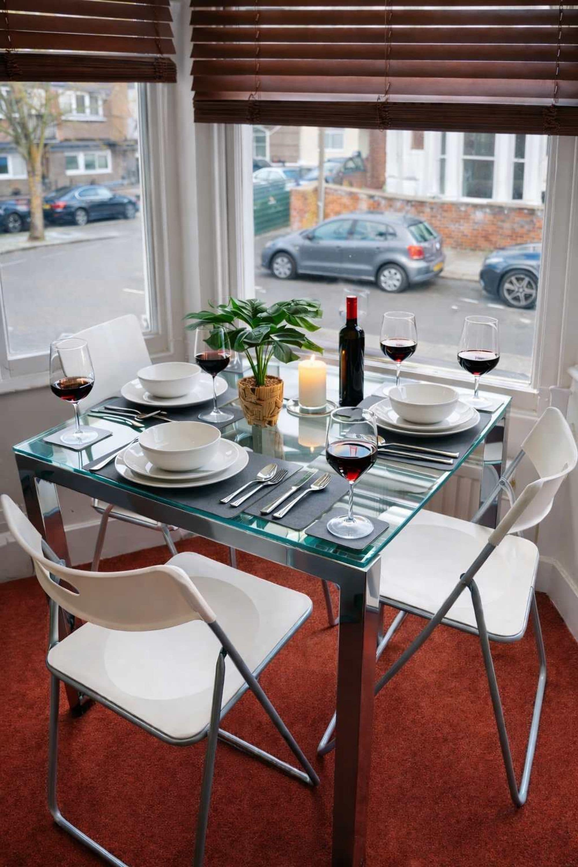 A dining table set for four with white chairs, a candle, and wine glasses.