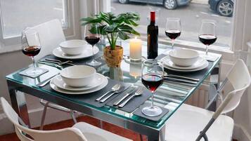 A dining table set for four with white chairs, a candle, and wine glasses.