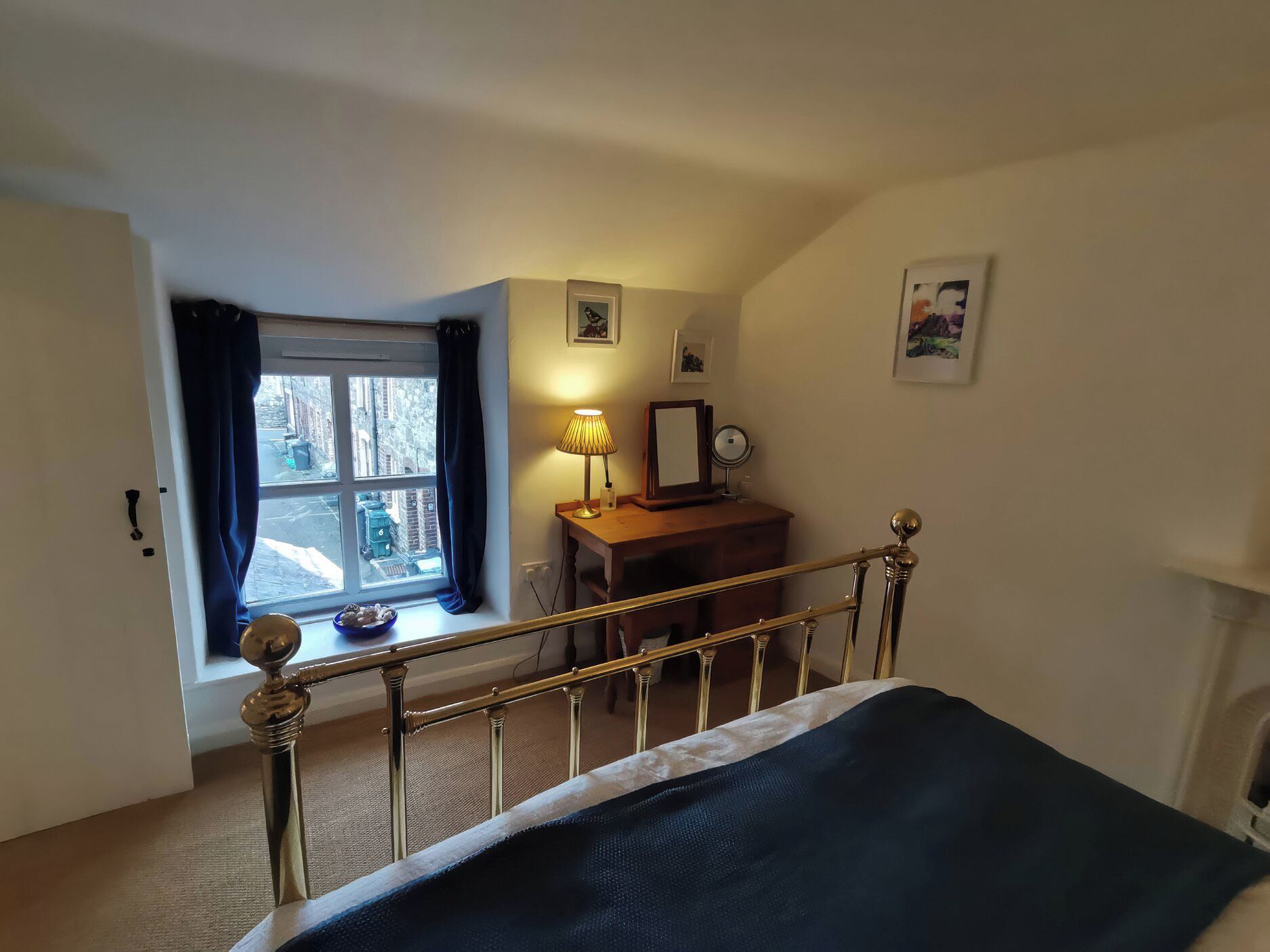 Une chambre à coucher avec un lit, un bureau avec une lampe, une fenêtre avec des rideaux et un tableau au mur.