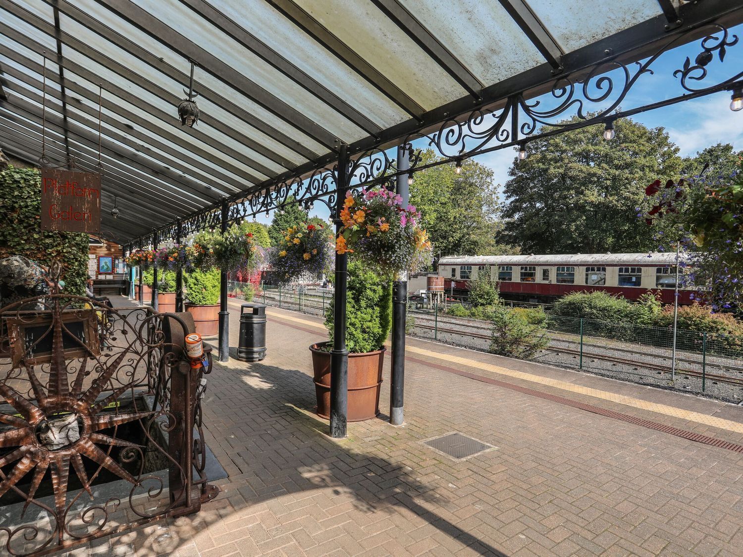 A covered outdoor seating area with metal railings and hanging flower baskets.