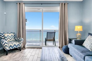 A room with a view of the ocean, a sofa, a chair, and a lamp. - Sterling Reef 505 (Panama City Beach)