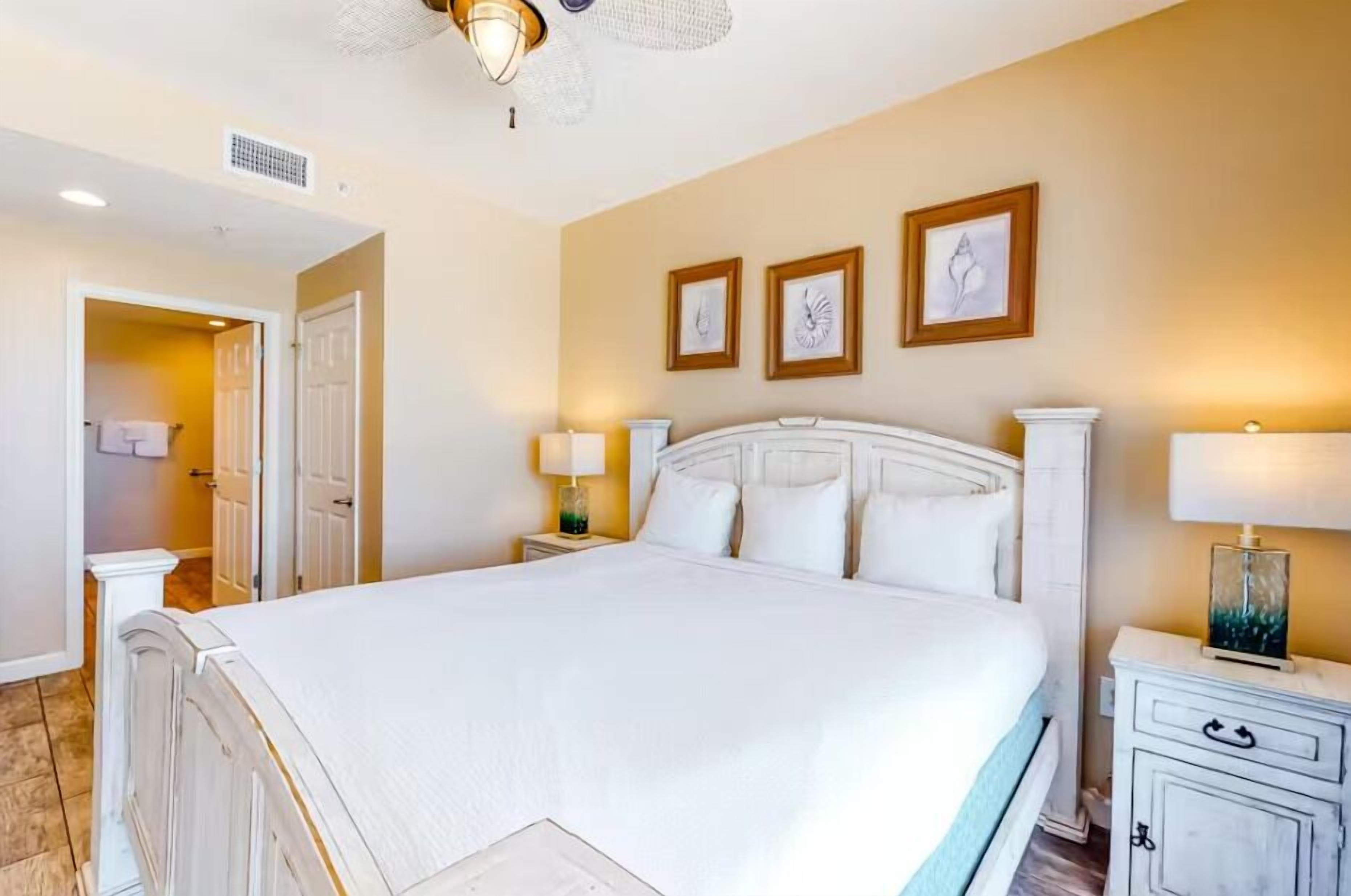 Un dormitorio espacioso con una cama grande, una mesita de noche con lámpara y una puerta que da a un baño.