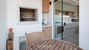 A modern kitchen with wooden cabinets, a built-in window shelf, and a glass door leading to the dining area. - Apt w/ BBQ Near the Beach in Pereque Fel0502 (Porto Belo)