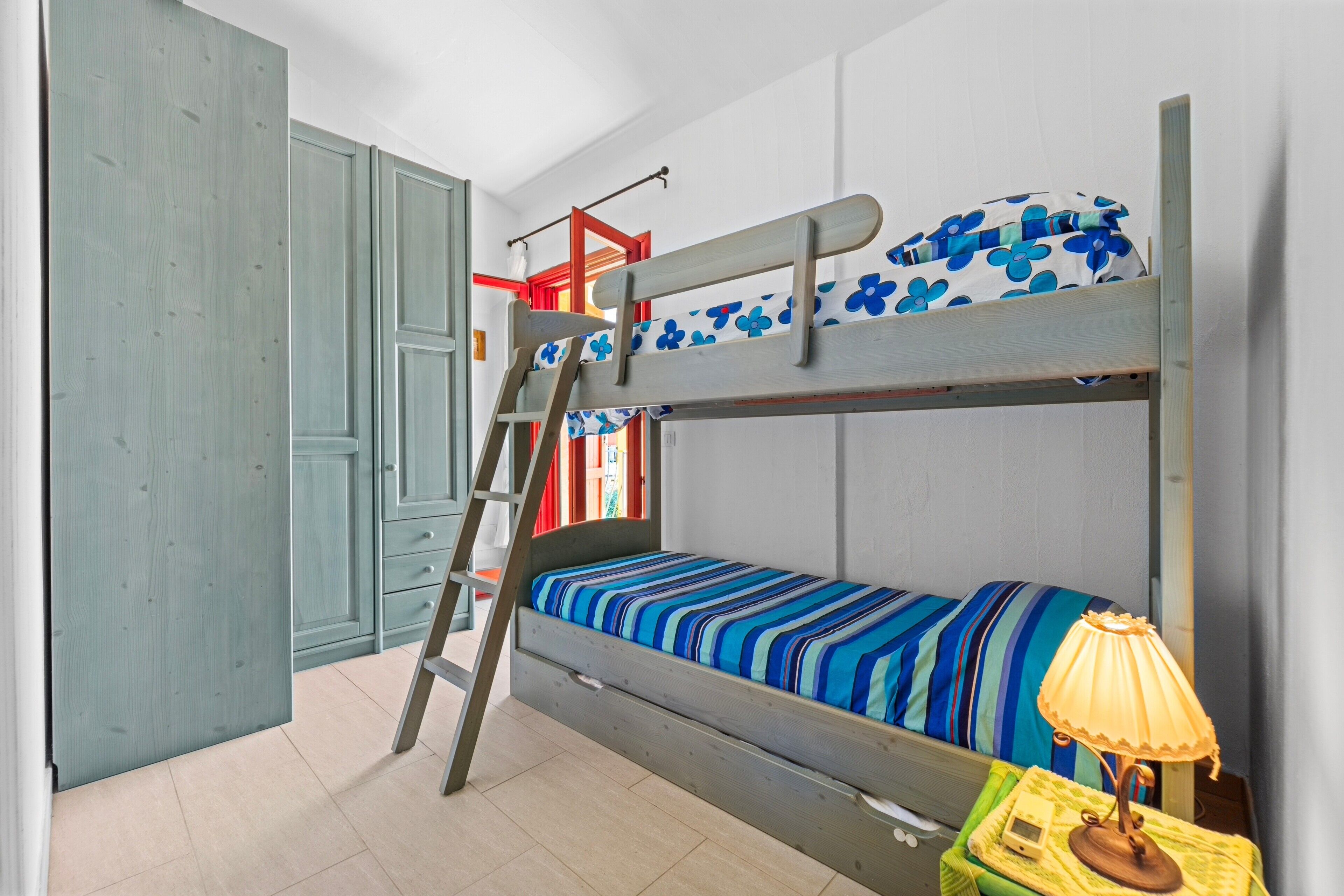 Un letto a castello con una scala, un piccolo tavolo con una lampada e un armadio.
