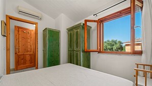 A bedroom with a bed, a wooden wardrobe, a green wardrobe, and a window with a view. - Villa 'Livia' with Shared Pool, Private Terrace and Garden (Sant'Anna Arresi)