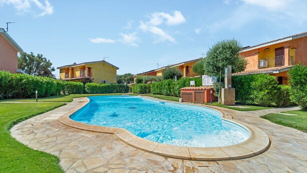 A swimming pool with a stone deck, surrounded by greenery and residential buildings. - Villa 'Livia' with Shared Pool, Private Terrace and Garden (Sant'Anna Arresi)